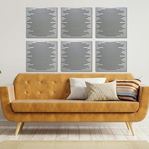 May include: Six silver sound-absorbing panels with a horizontal line pattern are arranged in a grid on a white wall above a brown couch with two pillows. The couch is in a living room setting with a potted plant on a side table to the right.