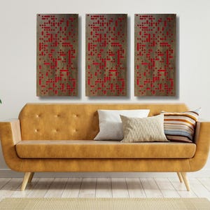 May include: Three rectangular wall art pieces with a wood grain background and a pattern of red squares. The art pieces are hanging on a white wall above a brown couch.