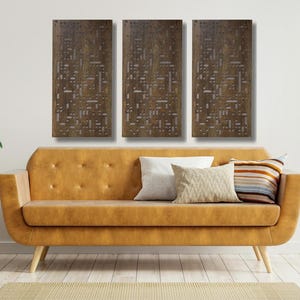 May include: Three brown wood wall panels with a geometric pattern cut out. The panels are hanging on a white wall above a brown leather couch with pillows.