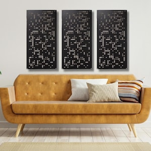 May include: Three black metal wall panels with a geometric pattern of white squares. The panels are hanging on a white wall above a brown leather sofa.