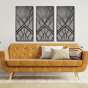 May include: Three black and white geometric wall art panels with a modern art deco design. The panels are hanging on a white wall above a brown leather couch.