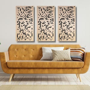 May include: Three beige wood panels with a black geometric pattern, hanging on a white wall above a brown couch with pillows.