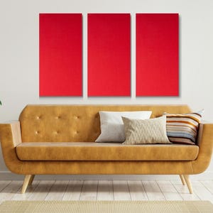 May include: Three red square canvases hang on a white wall above a brown leather sofa with pillows. The sofa is in a living room setting with plants and a side table.