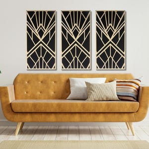May include: Three black and gold geometric art prints with a modern art deco design. The prints are hanging on a white wall above a brown couch with pillows.