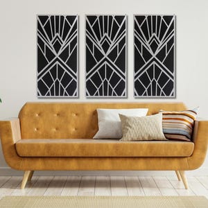 May include: Three black and white geometric art prints with a modern art deco design hang above a brown leather sofa with pillows.