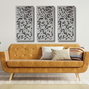 May include: Three rectangular wall panels with a geometric pattern of black squares on a silver background. The panels are hanging on a white wall above a brown couch with pillows.