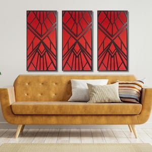 May include: Three red and black geometric wall art panels with a modern design. The panels are hanging on a white wall above a brown leather couch.