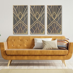 May include: Three rectangular wall art pieces with a geometric design in gold and gray. The art pieces are hanging on a white wall above a brown couch.