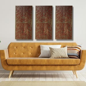May include: A modern living room scene featuring a mustard-colored sofa with decorative pillows. Above the sofa, three rectangular wall art pieces with a red geometric pattern are displayed. The room is decorated with plants and a wooden side table.