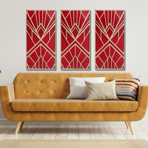 May include: Three red and gold art deco style wall panels hang above a mustard yellow sofa with pillows. The panels feature geometric designs. A plant in a white pot sits on a small wooden side table.