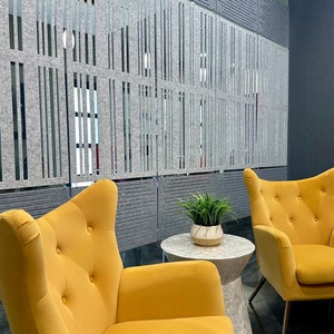 May include: Two yellow wingback chairs with button tufting and a small round marble side table with a potted green plant on top. The chairs are in front of a gray wall with a decorative panel.
