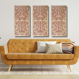 May include: Three rectangular wall art pieces with a geometric pattern of red squares on a cream background. The art is displayed above a brown couch in a living room setting.