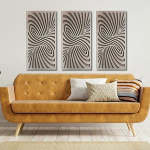 May include: Three abstract wall art panels with a swirling, striped pattern in shades of gray. The panels are hanging on a white wall above a brown couch.