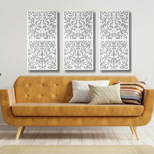 May include: Three white rectangular wall panels with a black dot pattern. The panels are hanging on a white wall above a brown leather sofa. The sofa has a light brown cushion and a striped cushion. There are two plants in pots on the floor.