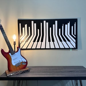 May include: A red electric guitar with a white pickguard and a black and white piano key design on the wall behind it.