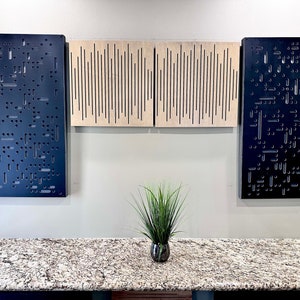 May include: Three black acoustic panels with different patterns of holes, mounted on a white wall. A small potted plant sits on a granite countertop below the panels.