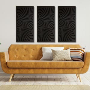 May include: Three black and white abstract wall art panels with a swirling pattern. The panels are hanging on a white wall above a brown couch with pillows.