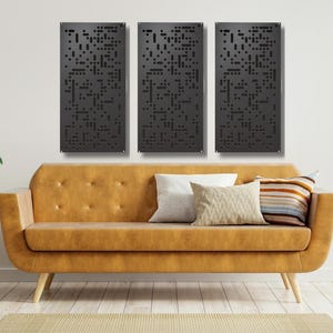 May include: Three black metal wall panels with a geometric pattern of small squares. The panels are hanging on a white wall above a brown leather sofa with pillows.
