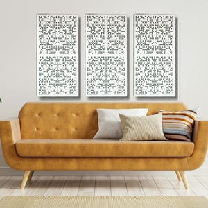 May include: Three white rectangular wall panels with a black geometric pattern. The panels are hanging on a white wall above a brown leather sofa.