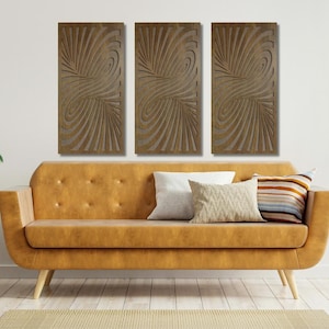 May include: Three brown wood wall art panels with a swirling, abstract design. The panels are hanging on a white wall above a brown leather couch.