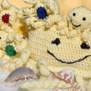 May include: A crocheted yellow octopus with a smiling face and black eyes. The octopus has several smaller crocheted octopus babies with colourful accents. The octopus is surrounded by seashells.
