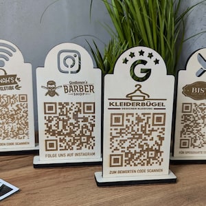 Könnte beinhalten: Vier Holzschildchen mit QR-Codes und Text. Die Schilder sind für ein Bastelstudio, einen Barbershop, ein Bekleidungsgeschäft und ein Bistro. Die Schilder stehen alle auf einem Holztisch.