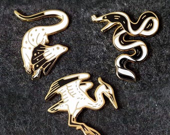 Broches de esmalte rígido com garça-cinzenta, enguia-fita e lagarto-de-gola.