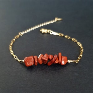 May include: A gold-toned chain bracelet featuring a central row of seven irregular, polished red jasper stone chips. The bracelet includes a delicate gold-coloured metal link chain with a lobster claw clasp and an adjustable extender chain at the end.