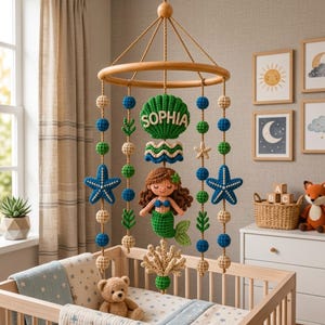 Pode incluir: Mobile para bebé feito à mão com um anel de madeira e elementos de crochê. O mobile inclui uma sereia, estrelas do mar e o nome "SOPHIA". As cores são azul, verde, bege e castanho. Pendurado sobre um berço.