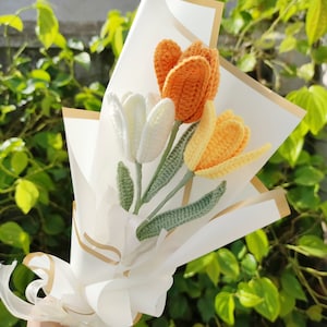 May include: A bouquet of crocheted tulips in white, orange, and yellow, wrapped in white paper with a gold ribbon.