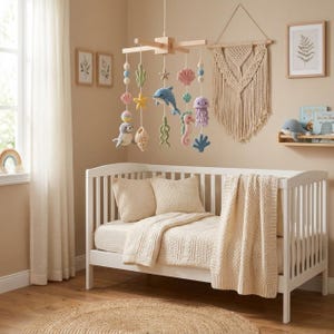 May include: A wooden baby mobile featuring crocheted sea creatures including a blue dolphin, pink seahorse, purple jellyfish, yellow starfish, and a gray seal, suspended from a light wood frame with colorful beads and shells.