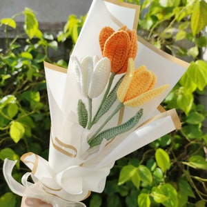 May include: A bouquet of crocheted tulips in white, orange, and yellow, wrapped in white paper with a gold ribbon.