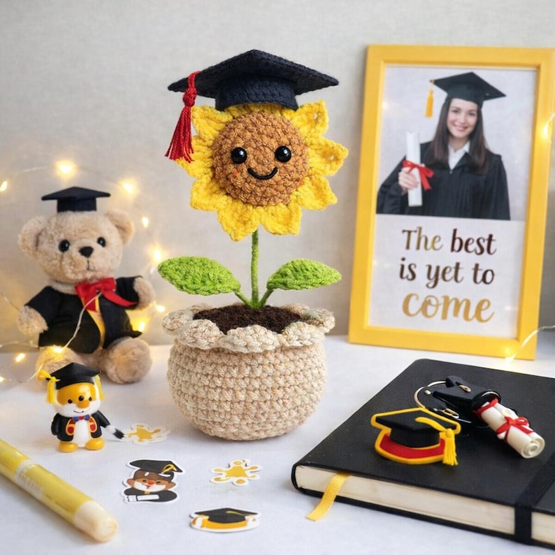 Puede incluir: Un girasol de ganchillo con birrete en una maceta beige. Tambi&eacute;n hay un oso de peluche con toga de graduaci&oacute;n y una foto enmarcada con el texto "The best is yet to come". Decoraci&oacute;n tem&aacute;tica de graduaci&oacute;n.