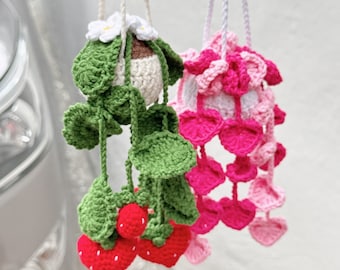 Op de afbeelding: Twee gebreide hangende planten, een met groene bladeren en rode aardbeien, de andere met roze en witte bloemen.