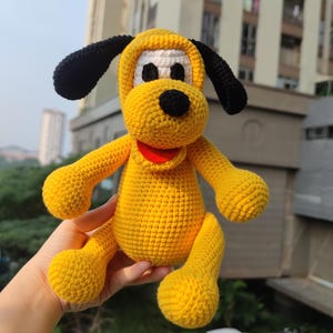 May include: A yellow crocheted plush toy dog with black ears and a red mouth. The toy has white eyes and a black nose.