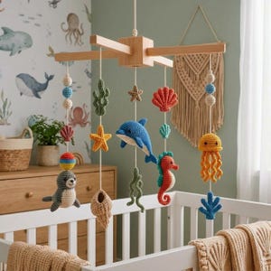 May include: A hanging nursery mobile featuring a wooden cross frame with various crocheted sea creatures and plants suspended by white strings, including a seal, dolphin, seahorse, jellyfish, starfish, seashells, and seaweed in colorful yarn.