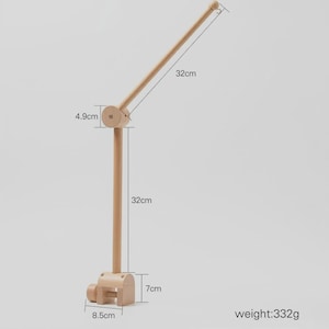 May include: A light-colored wooden mobile holder featuring a clamp base measuring 8.5 cm by 7 cm, a vertical rod measuring 32 cm, a 4.9 cm joint, and an angled arm measuring 32 cm. The total weight of the wooden structure is 332 grams.