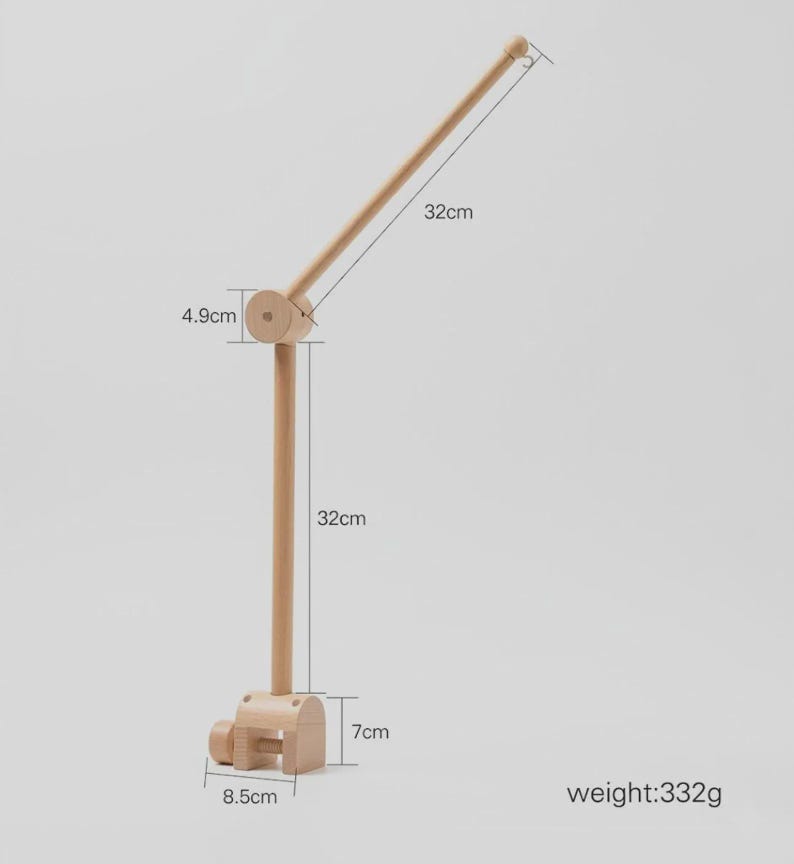 May include: A light-colored wooden mobile holder featuring a clamp base measuring 8.5 cm by 7 cm, a vertical rod measuring 32 cm, a 4.9 cm joint, and an angled arm measuring 32 cm. The total weight of the wooden structure is 332 grams.