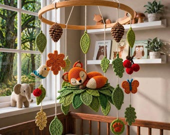 May include: A handcrafted baby mobile featuring a sleeping fox, leaves, and other woodland creatures. The mobile includes a wooden ring, crocheted leaves, a fox, a bird, a butterfly, and other decorative elements. The color palette includes shades of green, orange, brown, and white.