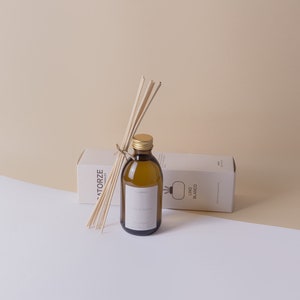 May include: A brown glass diffuser bottle with a gold cap, a bundle of wooden reeds, and a white box. The bottle has a label that reads "Lino Blanco". The box has the text "Catorze Candles".