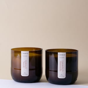 Puede incluir: Dos tarros de velas de vidrio marrón con etiquetas. La vela de la izquierda está etiquetada como "Violeta & Neroli" y la vela de la derecha está etiquetada como "Lavanda & Manzanilla". Ambas velas están etiquetadas como "Catorze Eco & Vegan" y "200 g Hecho a mano".