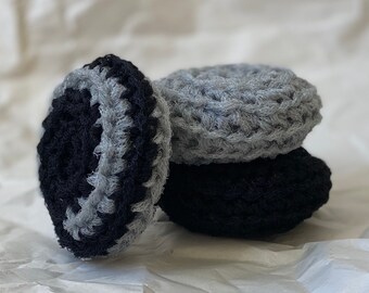 May include: Three crocheted scrubbers, one gray and two black, stacked on top of each other. The scrubbers are made of a soft, textured yarn.