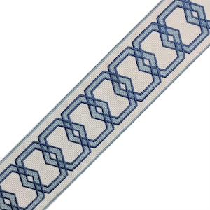 May include: Decorative ribbon featuring a repeating geometric pattern of interlocking blue octagons and diamonds. The design is embroidered on a light beige background with a pale blue border. The ribbon is angled across a white background.