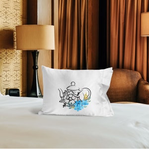 May include: White pillow with a black line drawing of a teapot with blue and yellow flowers.