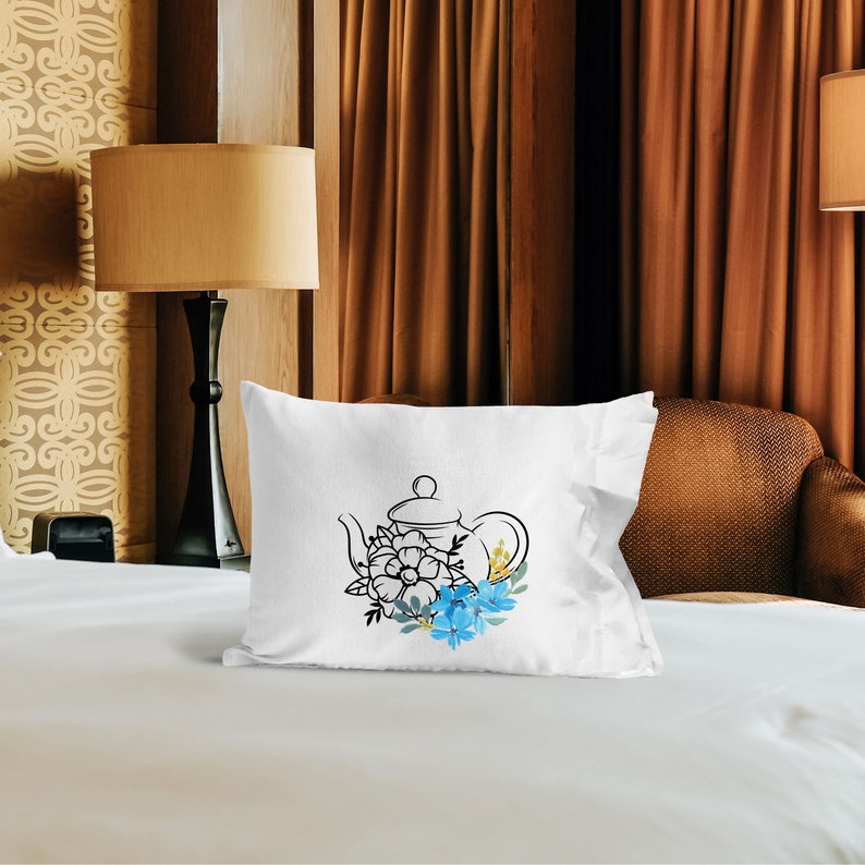 May include: White pillow with a black line drawing of a teapot with blue and yellow flowers.