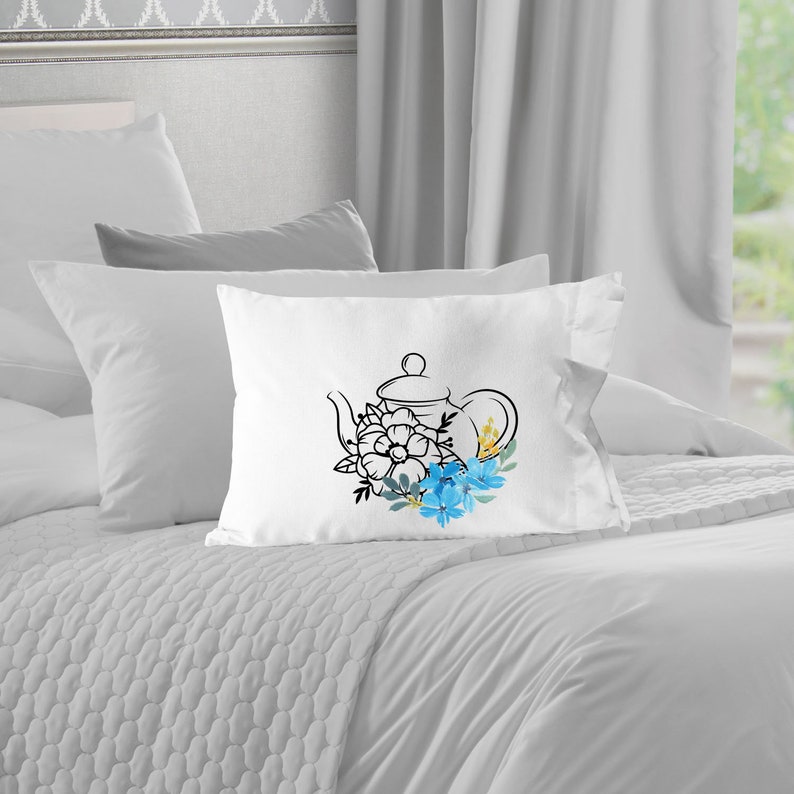 May include: White pillow with a black line drawing of a teapot with blue and yellow flowers.