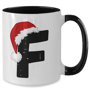 Può includere: Tazza in ceramica bianca con manico e interno neri. La tazza presenta la lettera "F" nera con un design a cappello di Babbo Natale. Il cappello di Babbo Natale è rosso con finiture bianche e un pompon bianco.