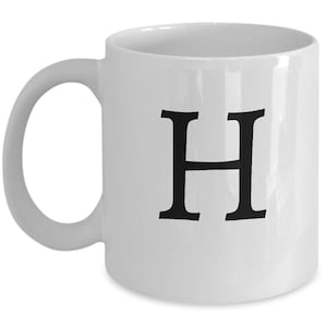 Puede incluir: Taza de café de cerámica blanca con una letra H negra impresa en la parte delantera.