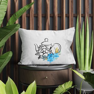 May include: White pillow with a black line drawing of a teapot with blue and yellow flowers.