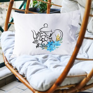 May include: White pillow with a black line drawing of a teapot with blue and yellow flowers.